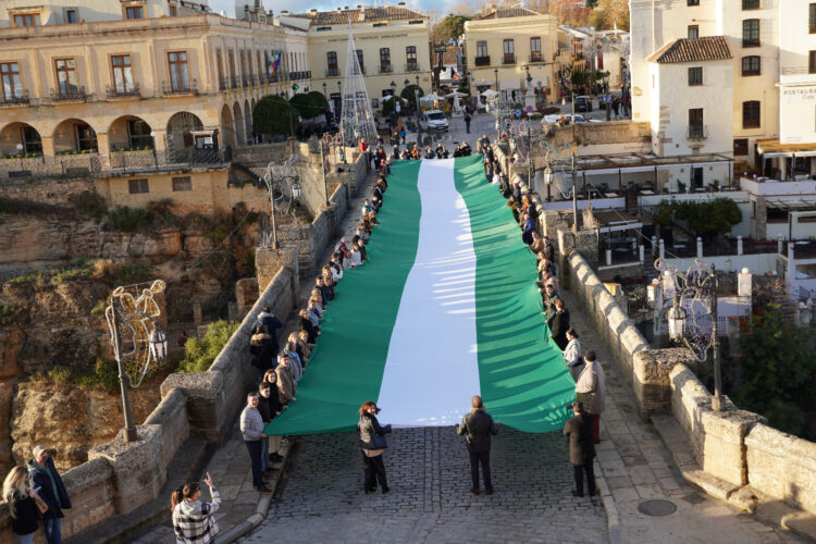 El PP de Málaga celebra el 4D desplegando una gran bandera andaluza en el Puente Nuevo